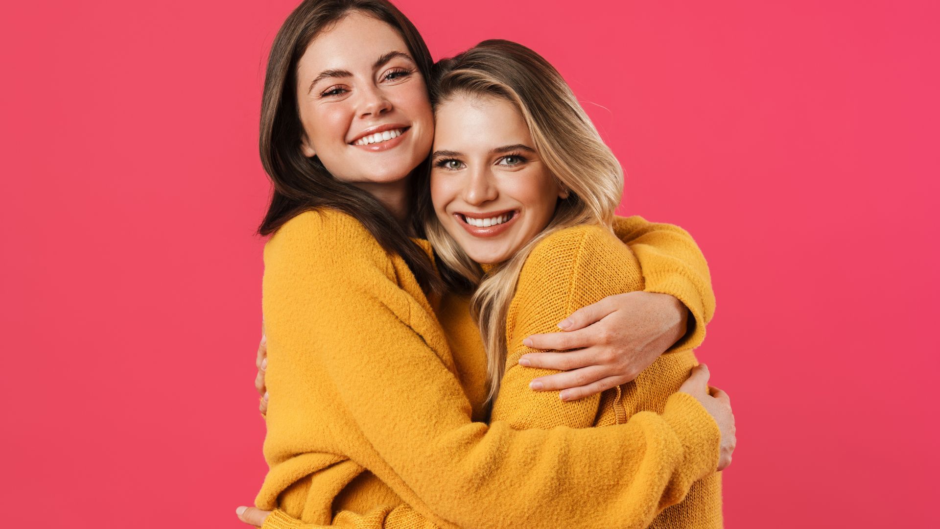 Masajes para dos amigas. Dos amigas con sueters iguales abrazadas y sonriendo a cámara.