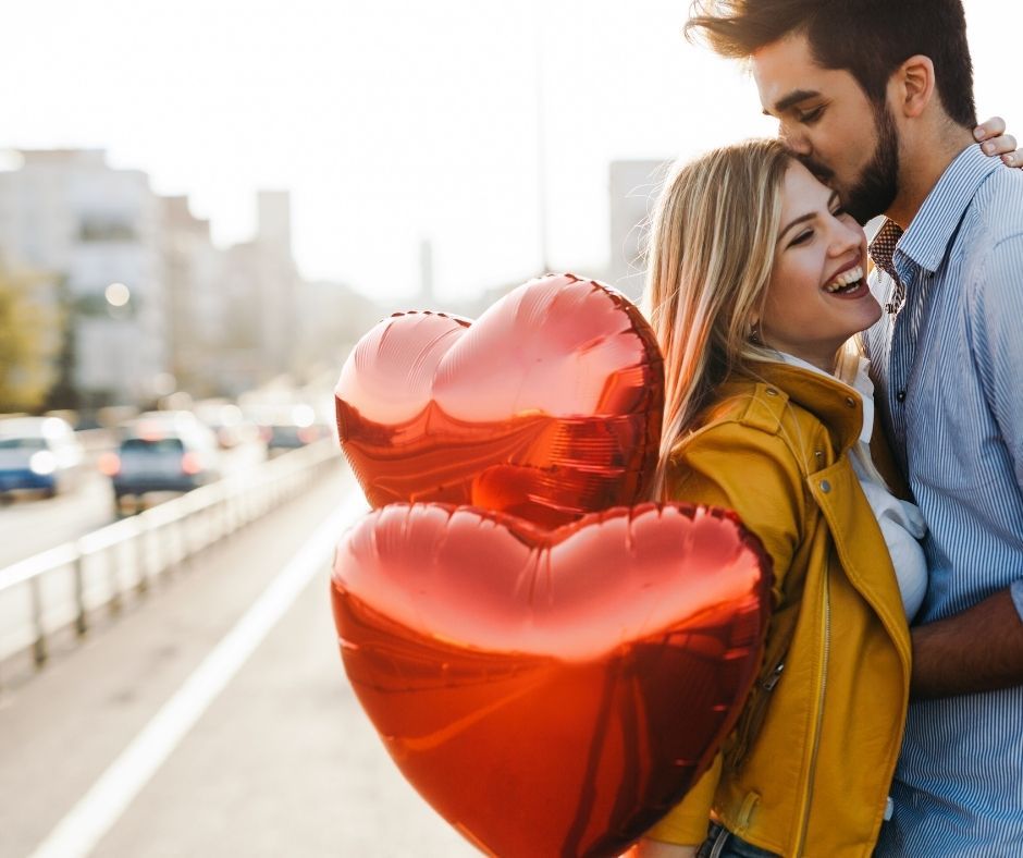 Celebra san Valentin con un masaje en pareja. Pareja abrazándose en la calle, mientras sujetan globos en forma de corazón