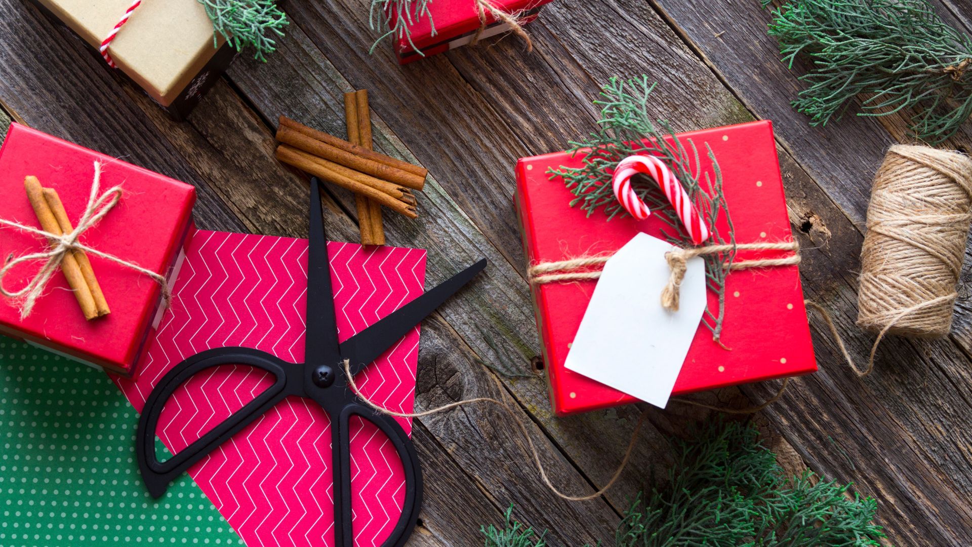 Mesa de madera con papel de regalo tijeras y varios regalos ya envueltos con simbología navideña