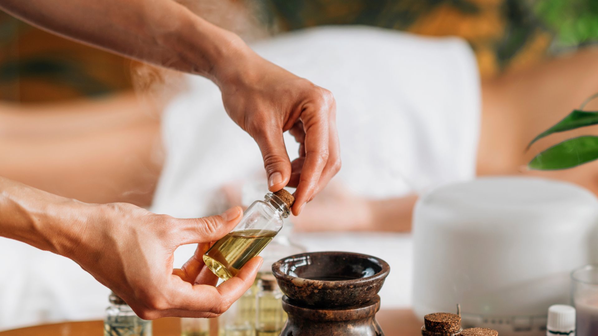Masajista preparando frangancia spa de aromaterapia mientras el cliente espera tumbado boca abajo en la camilla