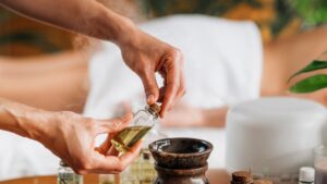 Masajista preparando frangancia spa de aromaterapia mientras el cliente espera tumbado boca abajo en la camilla